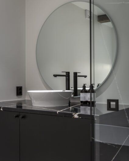 Minimalistisk bad med rundt speil og benkeplate av marmor, utført av Lomundal.