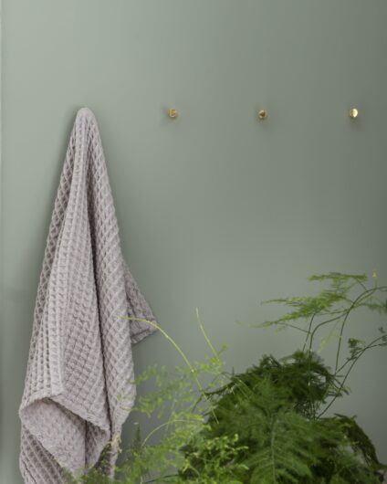 Detaljbilde av bad med grønne vegger, knotter i messing og grønn plante, utført av Lomundal.
