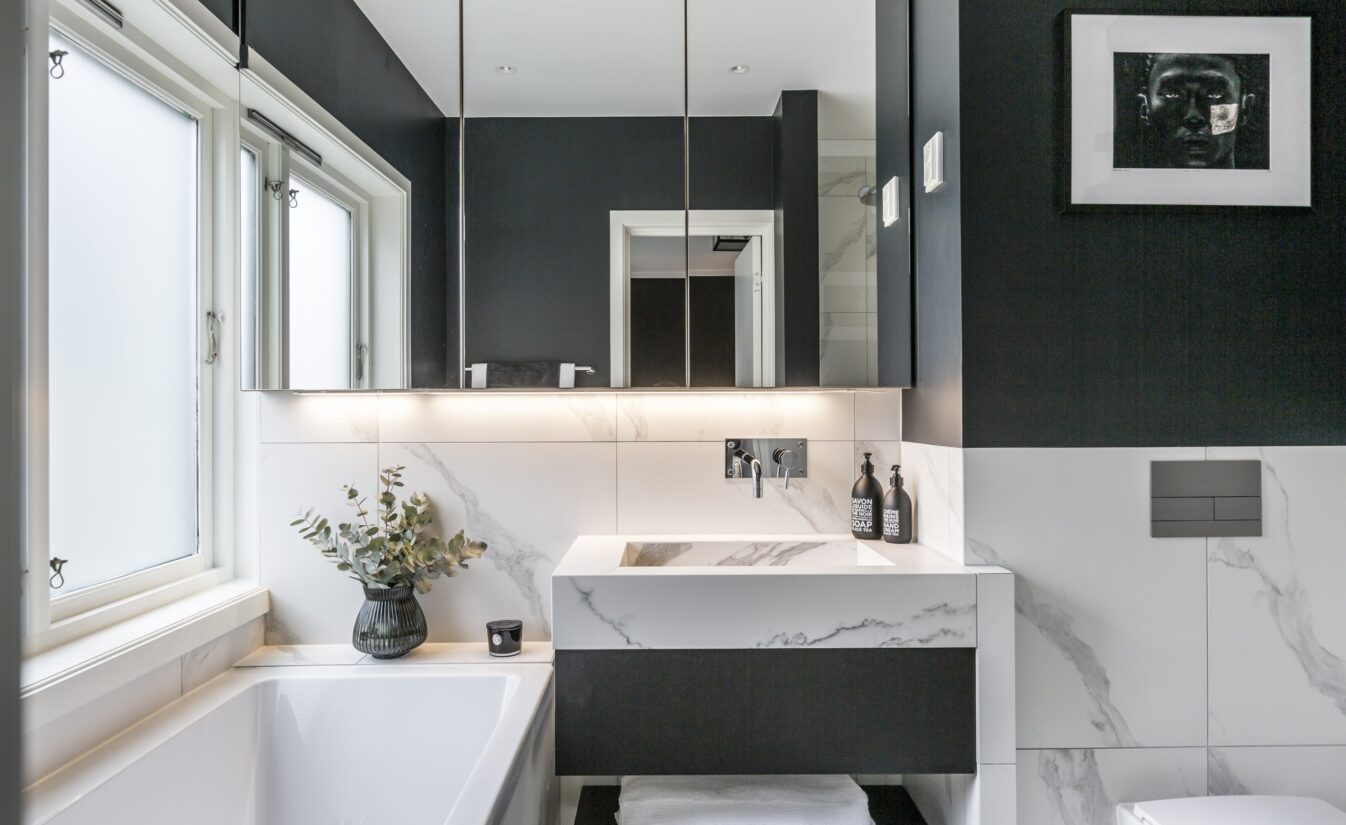 Baderom med badekar og lyse fliser med kontrastvegg i mørk grå, utført av Lomundal.