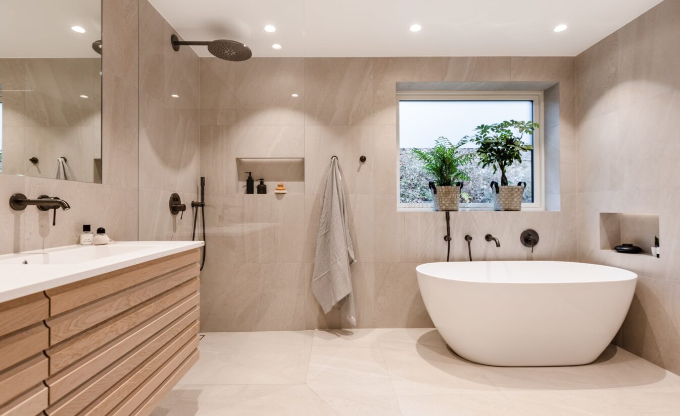 Baderom med frittstående badekar. Til venstre for badekaret er det en dusj og ovenfor det står baderomsinnredningen med dobbel vask.