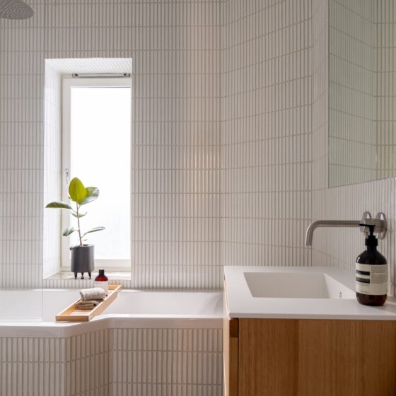 Bad med innebygd badekar, små avlange hvite fliser på vegg, innebygde armaturer i stål. Pusset opp av Lomundal.