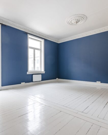 Tom stue før oppussing med hvitmalt furugulv, mørke blå malte vegger.
