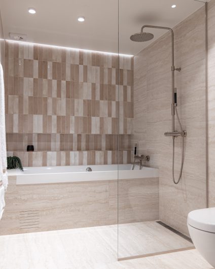 Baderom pusset opp med dusj og innebygd badekar. Lys travertinflis på gulv og vegg samt kontrastvegg med mindre flis over badekar.