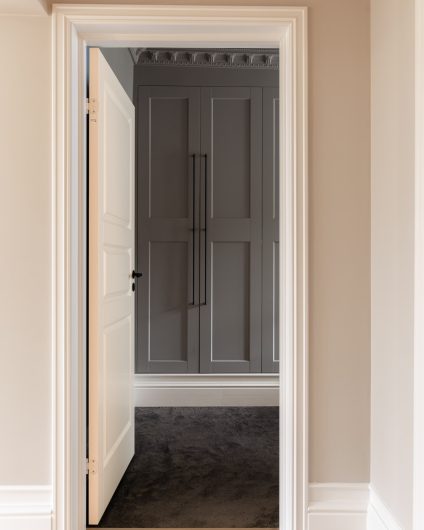 Fra gang inn til soverom i leilighet i klassisk stil. Soverommet har gulvteppe og innebygd garderobe.