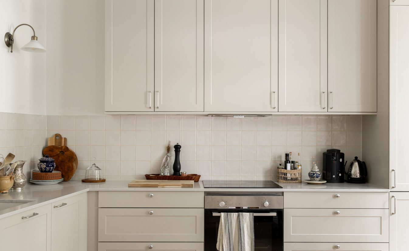 Et lyst og moderne kjøkken i klassisk stil. På veggen er det lagt blanke fliser med ujevne kanter og en bølgete overflate som tilfører personlig preg på kjøkkenet. Utført av Lomundal.