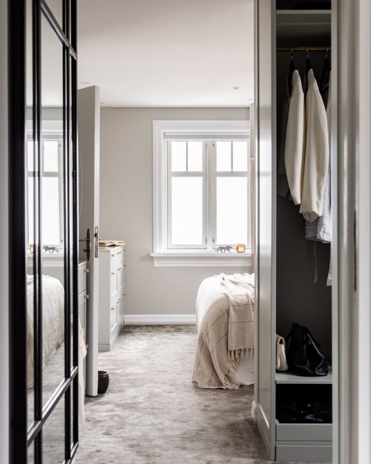 Master soverom med vegg-til-vegg teppe på gulv, spesialbygd garderobe og lyse toner på vegg. Utført av Lomundal.