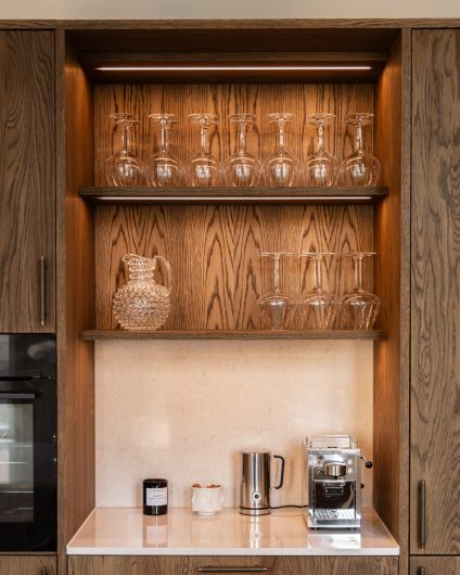 Elegant kjøkken i mørkt treverk med en lys benkeplate og backsplash i kompositt. Utført av Lomundal.