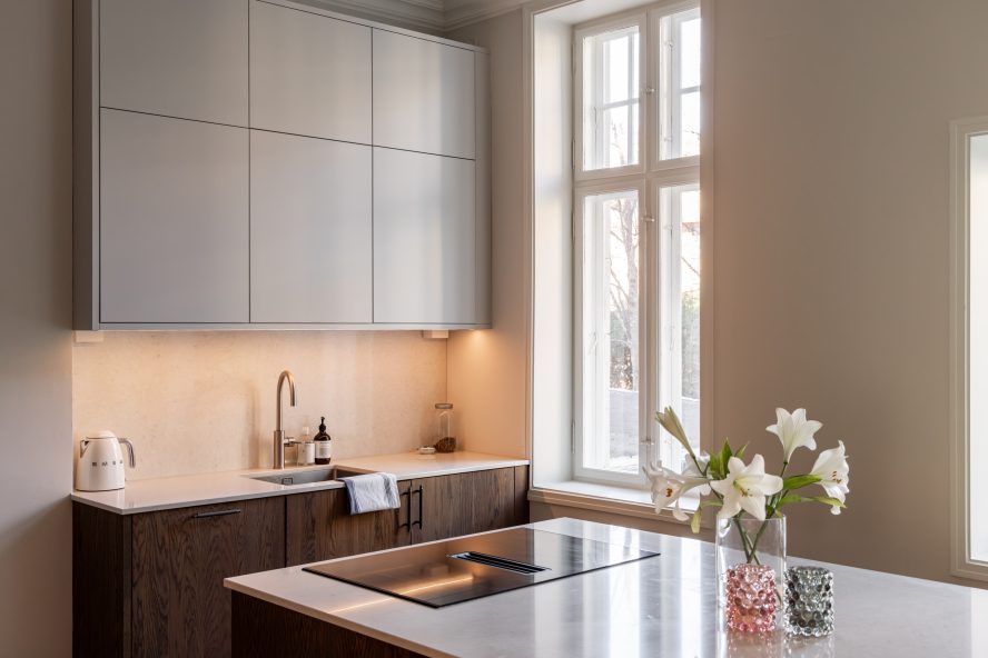 Et moderne, skandinavisk kjøkken i mørkt treverk med en lys benkeplate i kompositt. Kjøkkenet har en stor kjøkkenøy som gir godt med arbeidsplass. Utført av Lomundal.