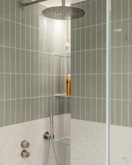 Dusjsone med blanke, smale fliser og terrazzofliser. Badet har et naturlig og skandinavisk preg i duse grønntoner. Utført av Lomundal.