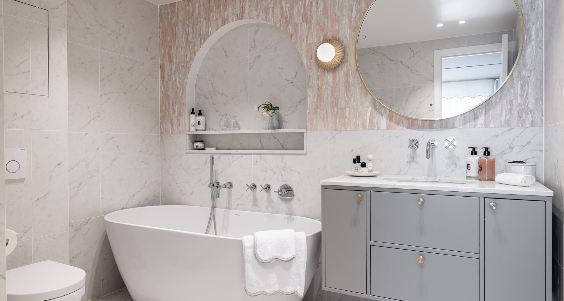 Eksklusivt, klassisk bad i lyse, delikate fargetoner. Badet er flislagt med norsk, rosa Fauske marmor og Carrara marmor. Badet har et frittstående badekar og en buet dusjnisje på vegg. Utført av Lomundal.