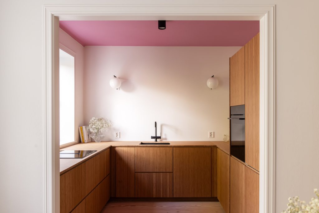 Lyst kjøkken med kjøkkeninnredning i bambus, vegger malt i klassisk hvit, og tak malt i en lekker rosafarge.