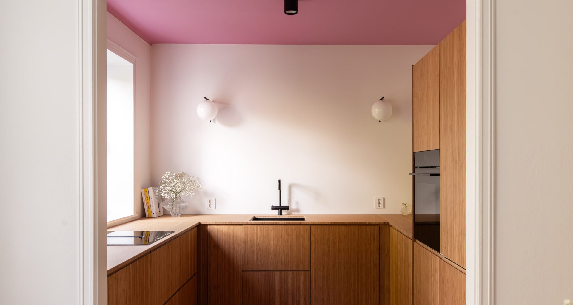 Lyst kjøkken med kjøkkeninnredning i bambus, vegger malt i klassisk hvit, og tak malt i en lekker rosafarge.