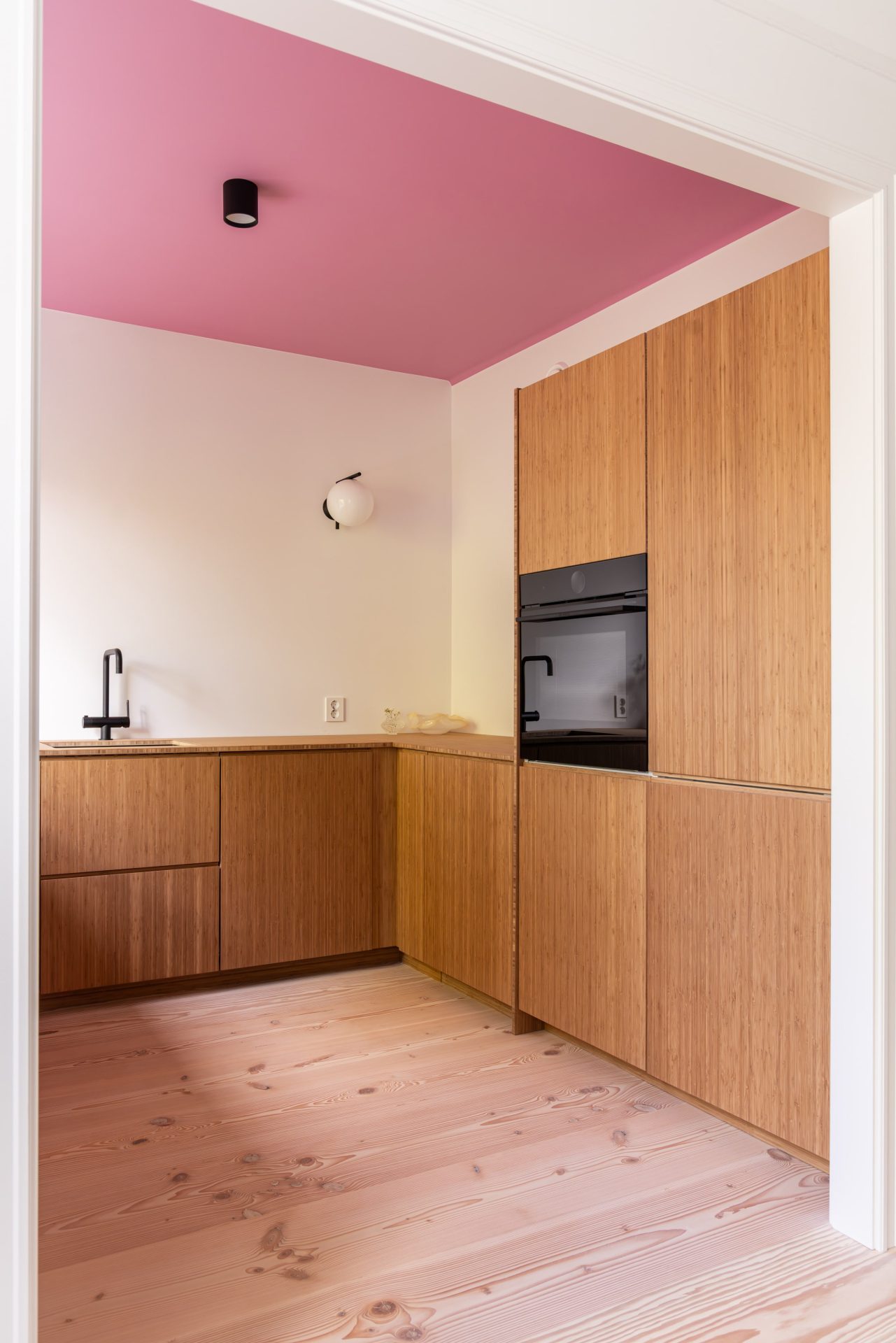 Lyst kjøkken med kjøkkeninnredning i bambus, vegger malt i klassisk hvit, og tak malt i en lekker rosafarge. - Bilde