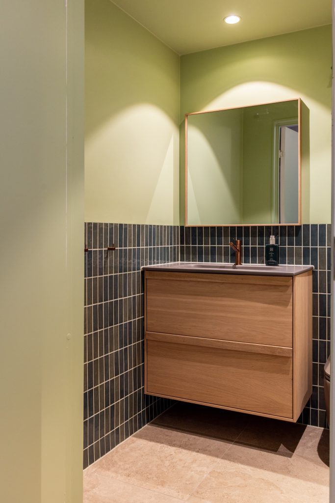 Lyst bad i friske farger. Badet kombinerer beige nyanser med lyst treverk, og vegger i grønntoner. Et moderne, nyoppusset bad med personlig uttrykk. Utført av Lomundal.