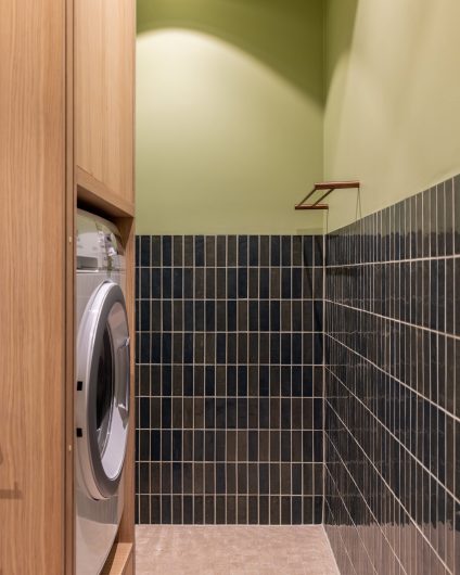 Plassbygd høyskap fra møbelsnekker i lys eik på moderne bad. Skapet har oppbevaringsmuligheter, skyvedør og rom for vaskemaskin.