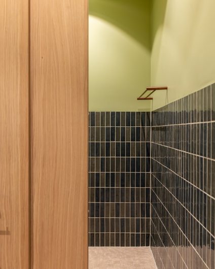 Moderne bad i grønntoner med en romslig dusjsone. På gulvet er det små kvadratiske beige fliser. På veggen er det smale blanke fliser i en dyp grønnfarge kombinert med malte flater.