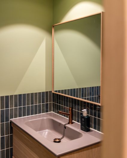 Bad i ulike grønntoner med baderomsinnredning i lys eik og servant i bruntoner. Badet har et naturlig fargepalett, samtidig som det fremstår fargerikt.