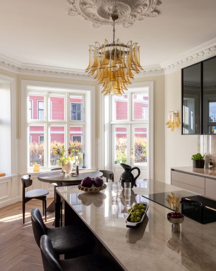 Kjøkken i beigetoner som kombinerer en moderne og klassisk stil. Kjøkkenet har et elegant uttrykk med eksklusive materialer, og hint av klassiske elementer som rosett i taket, stukkaturlister og fiskebensparkett. Utført av Lomundal.