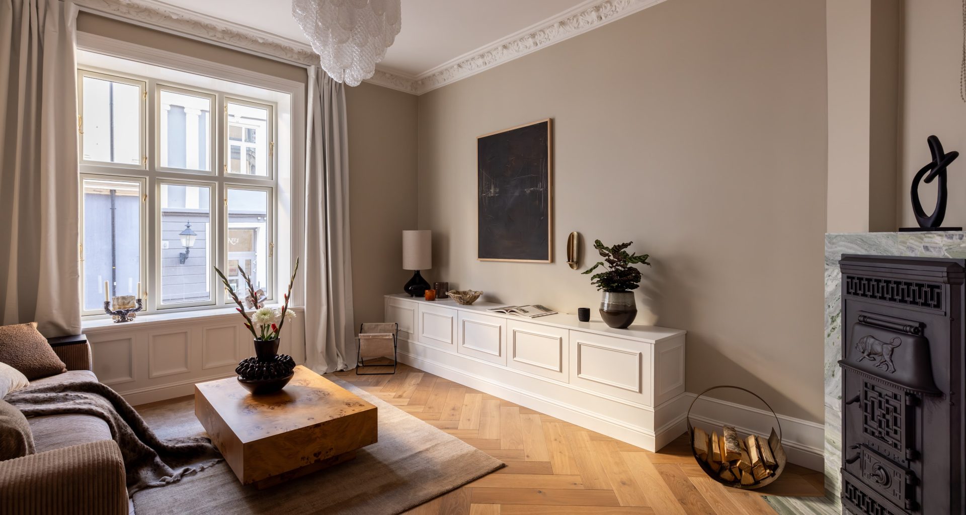 Klassisk stue i beigetoner med elegante stukkaturer, fiskebensparkett og en peis innrammet i blågrønn naturstein. Utført av Lomundal.