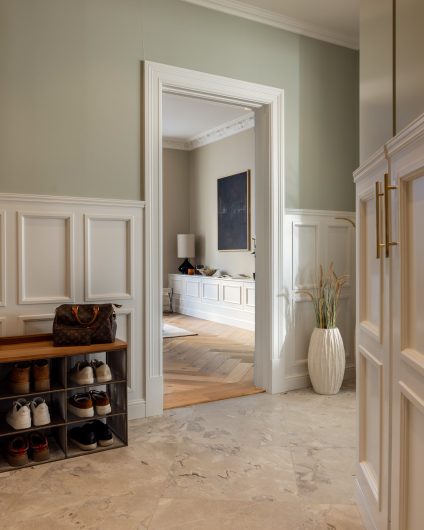 Klassisk gang i lyse fargetoner, stukkaturlister på vegg og fliser med et spill og variasjoner i mønsteret. Utført av Lomundal.