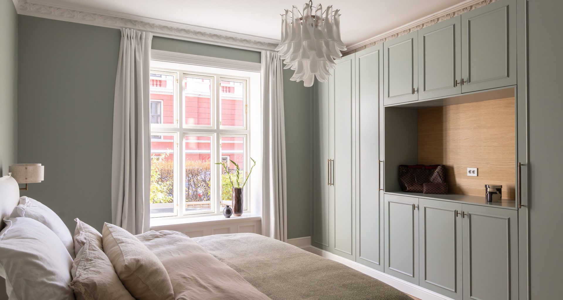 Klassisk soverom i en dus grønnfarge med hvite, elegante stukkaturlister og rosett. Rommet har en behagelig og lys atmosfære, med detaljer i lyst treverk og plassbygd skap. Utført av Lomundal.