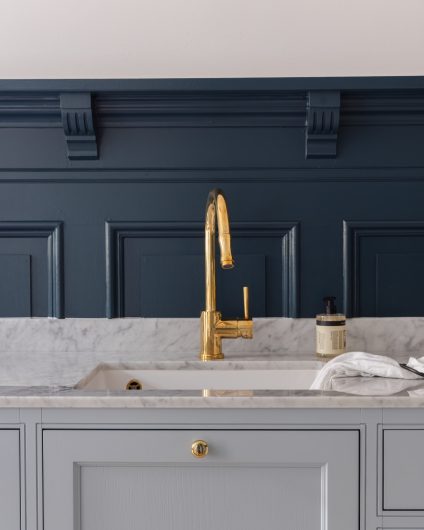 Detaljbilde av kjøkkeninnredning og vask på et kjøkken i klassisk stil. Kjøkkenet er i ulike blå nyanser, og har detaljer i messing. Utført av Lomundal.