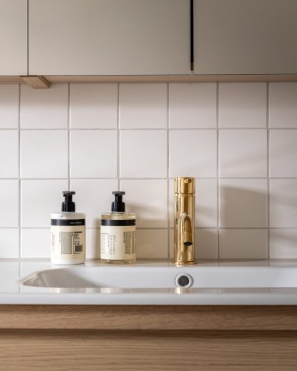 Tidløst bad i lyse toner med baderomsinnredning i eik og armatur i oksidert messing. Utført av Lomundal.