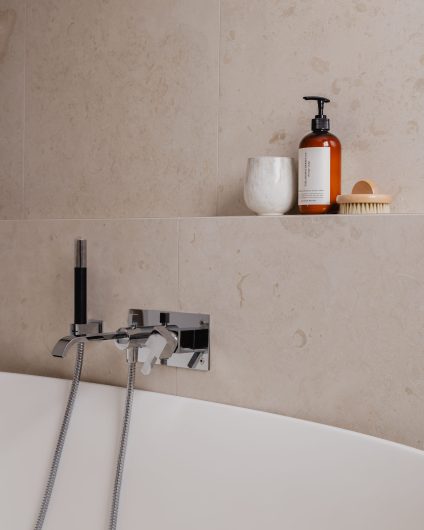 Detaljbilde av frittstående badekar og store beige fliser med naturlig mønster. Totalrenoveringen er utført av Lomundal.