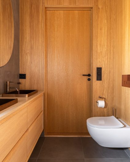 Moderne bad som kombinerer kalde, mørke fliser med varm eikefinér på vegg og baderomsmøbler i mørkt tre. Utført av Lomundal.