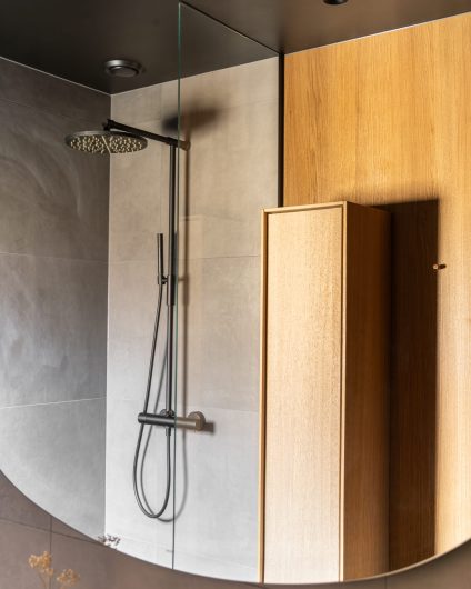 Mørkt bad med grå fliser i dusjsonen og eikefinér på resterende vegger. Utført av Lomundal.