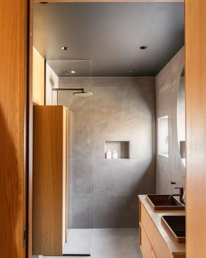 Mørkt bad med grå fliser og innredning i lys eik. Utført av Lomundal.