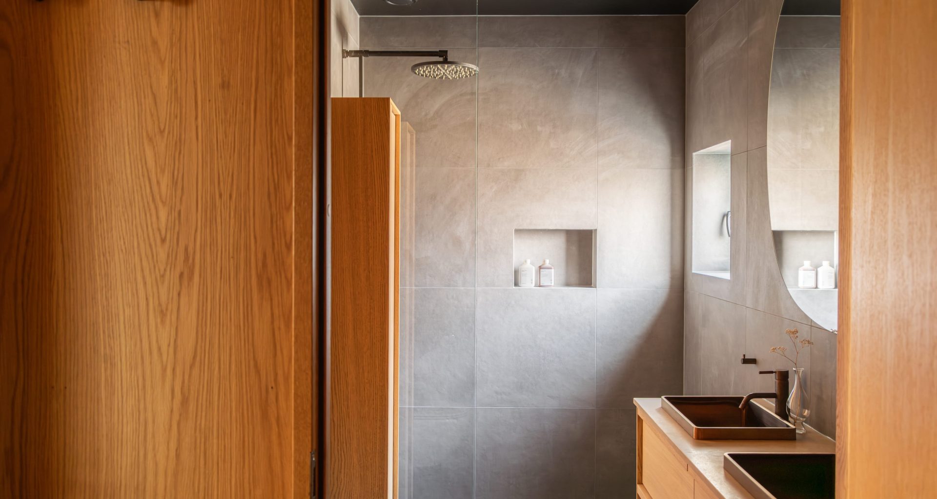 Mørkt bad med grå fliser og innredning i lys eik. Utført av Lomundal.