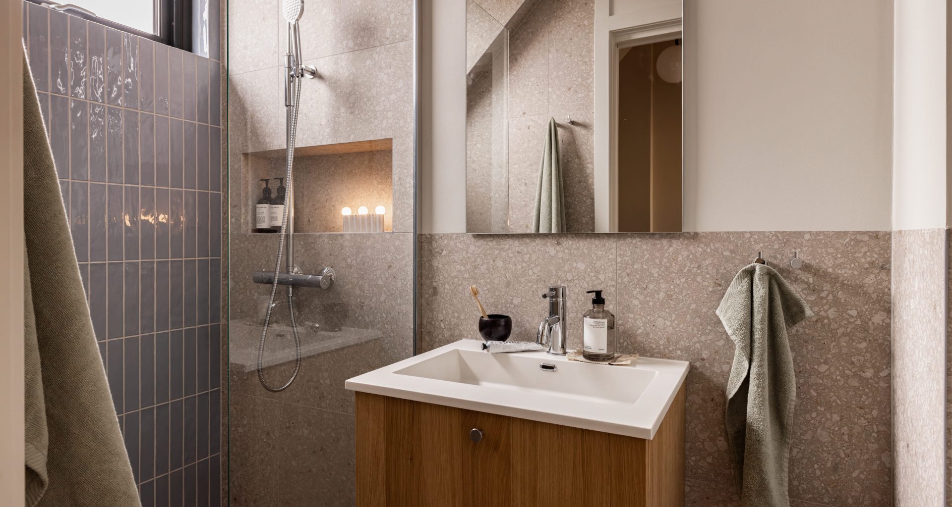 Skandinavisk bad med blå, blanke fliser i dusjsonen, terrazzoflis på gulv og vegger og baderomsinnredning i lyst treverk med armaturer i krom. Badet er totalrenovert av Lomundal.