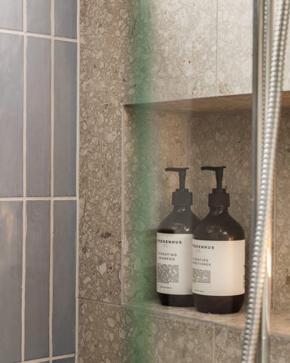Dusjsone med blå, blanke fliser og terrazzo på vegg, med en liten dusjnisje til oppbevaring av dusjartikler. Badet er totalrenovert av Lomundal.