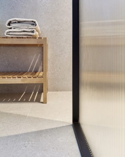 Bad med dusjvegg med rillet glass og beige, store fliser på gulv og vegger, med innredning i treverk. Utført av Lomundal.