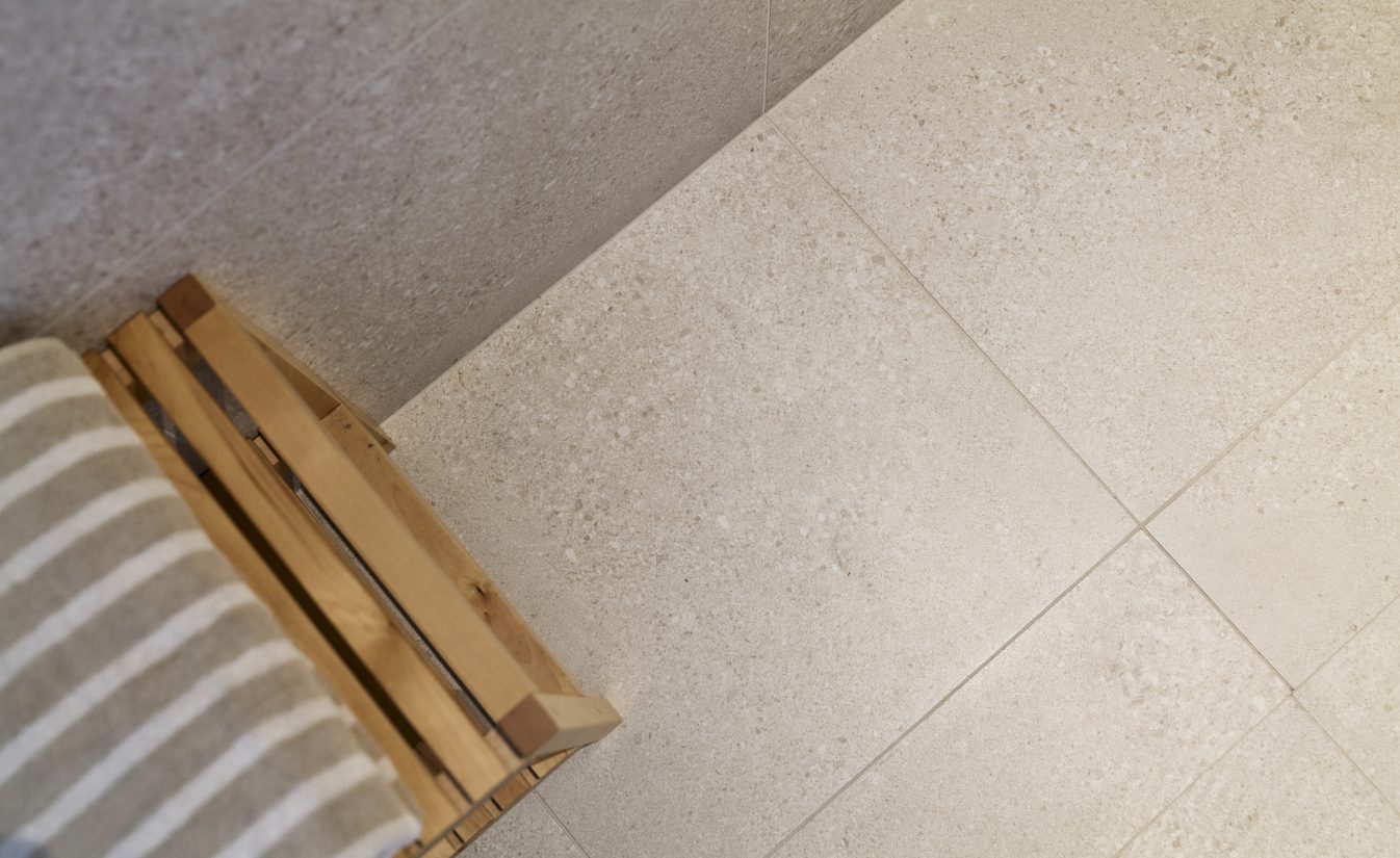 Baderomsgulv med store, beige fliser som gir et naturlig og rolig uttrykk. Utført av Lomundal.