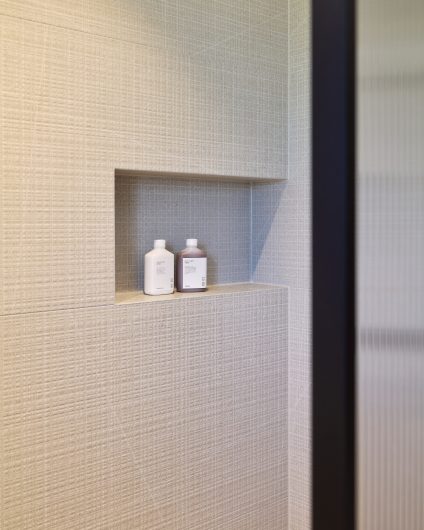 Detaljbilde av dusjsone med dusjnisje og organiske, beige fliser. Utført av Lomundal.