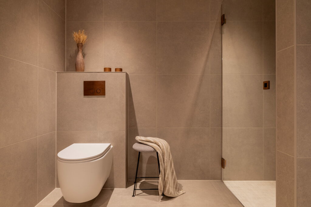 Totalrenovering av bad i moderne stil med et skandinavisk preg. Kunden ønsket et tidløst bad med beige fliser og armaturer i børstet kobber, for et varmt og gyllent uttrykk. Utført av Lomundal.