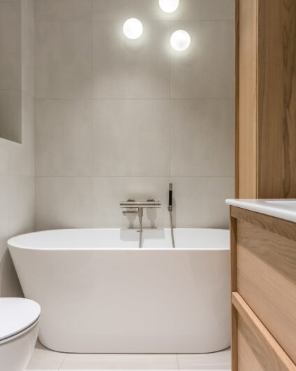Detaljbilde fra bad med lyse fliser, hvitt badekar og tre vegglamper montert med usymmetrisk plassering, utført av Lomundal.