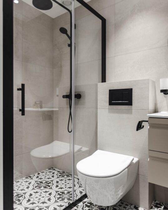 Bad med tradisjonelle fliser på gulv, lyse kvadratiske fliser på vegg, detaljer og armaturer i matt sort og hvitt toalett. Badet er totalrenovert av Lomundal.