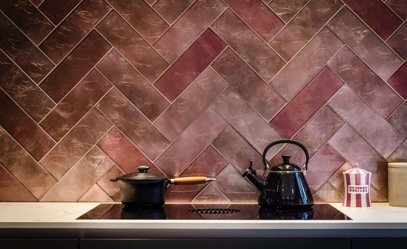 Detaljbilde av kjøkken med rosa chevronfliser på vegg. På kokeplaten står en gryte og en vannkoker. Kjøkkenet er totalrenovert av Lomundal.