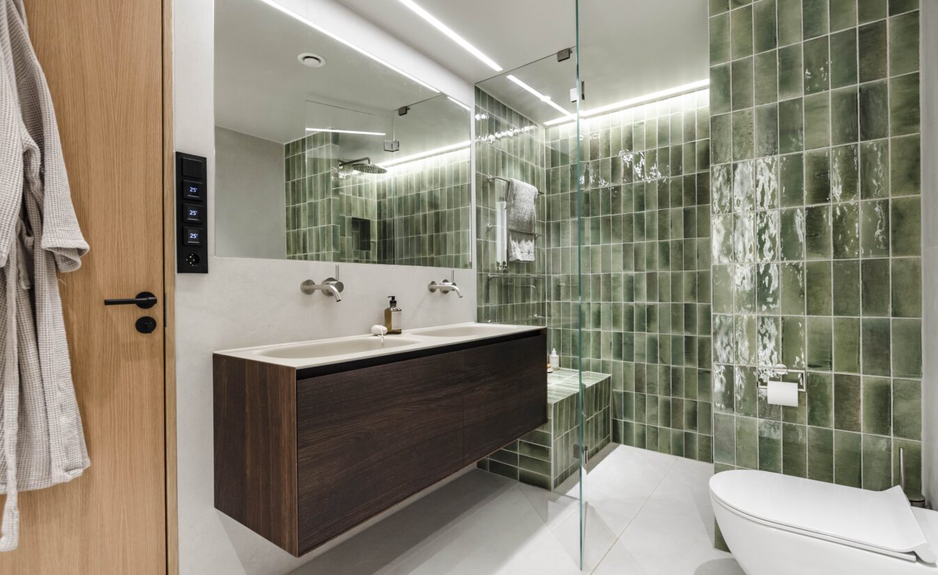 Baderom med grønne vannrette fliser i dusjsonen, lyse fliser på resten av vegg og gulv og baderomsinnredning i mørkt treverk.