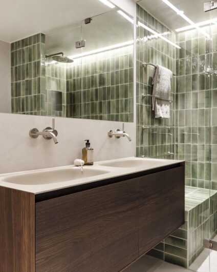 Baderom med grønne vannrette fliser i dusjrom, baderomsinnredning med nedfelt dobbelt vask og innebygde armaturer fra Dornbracht. Spesialtilpasset speil over.