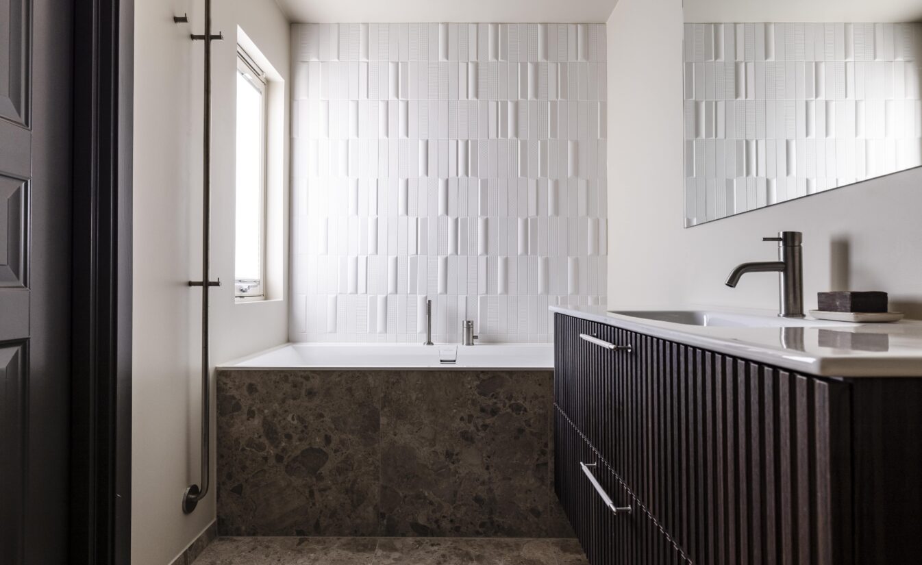 Moderne baderom med fliser på gulv og rundt badekar i beige stein. Over badekaret er det lagt 3D dimensjonale fliser. Utført av Lomundal.