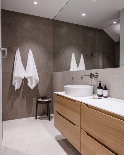 Moderne bad med store grå fliser, baderomsinnredning i eik og frittstående vask. Utført av Lomundal.