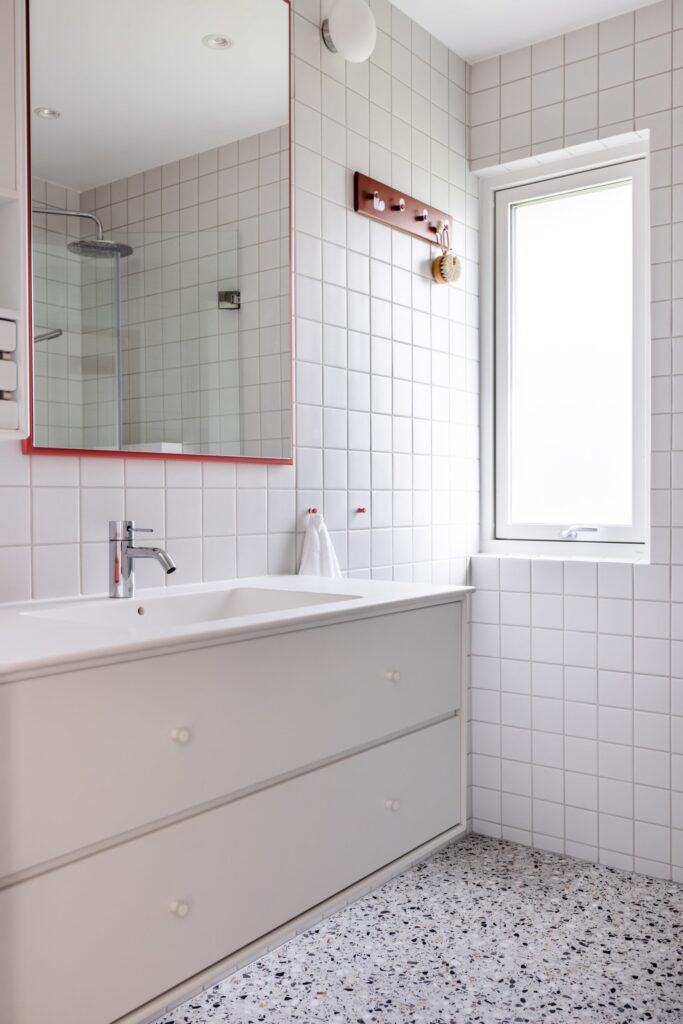 Retro bad med terrazzo fliser på gulv og kvadratiske fliser på vegg. Gjennomført med røde detaljer. Utført av Lomundal.
