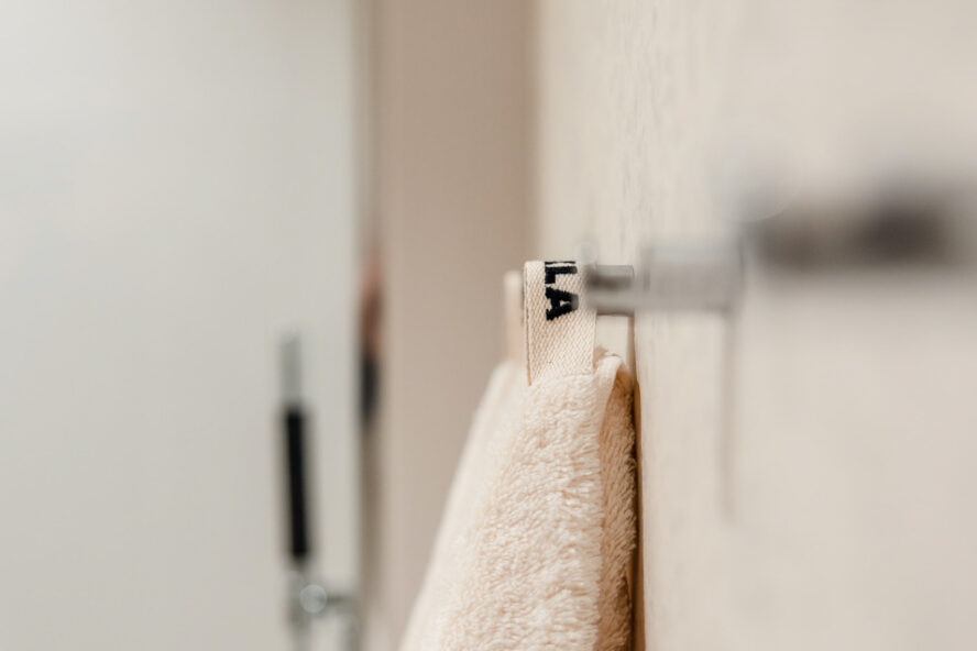 Detaljer på lyst og moderne bad med store lyse fliser på vegg. Vegghengte knagger til håndklær fra Tekla. Badet er pusset opp av Lomundal.
