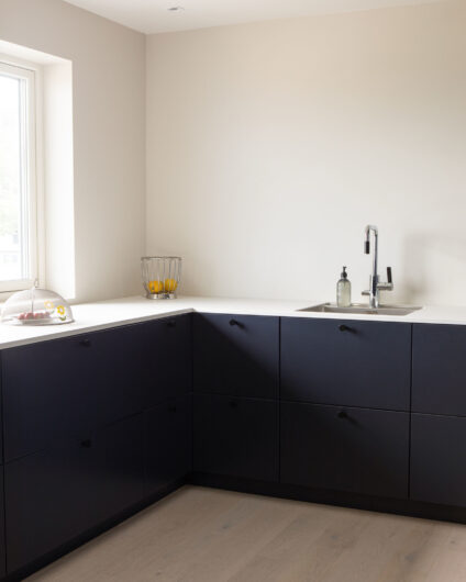 Moderne kjøkken fra Drømmekjøkkenet med sorte fronter og lys benkeplate. Lyse vegger og minimalistisk uttrykk.