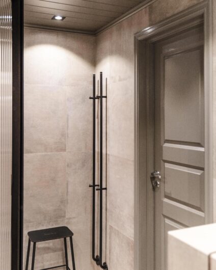 Moderne bad med varme grå fliser, panel i tak og sorte detaljer. Utført av Lomundal.