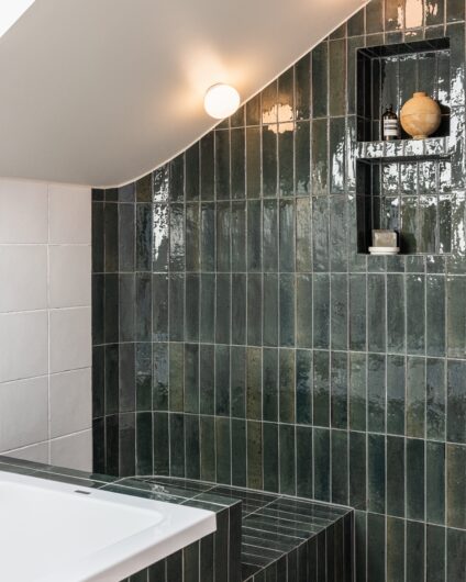 Avlange grønne fliser med glans lagt rundt badekar og dusj. To hyllenisjer er bygd inn i veggen ved dusjen. Utført av Lomundal.